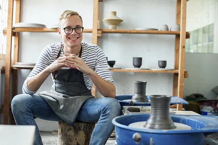 A man sits happily beside his pottery wheel.