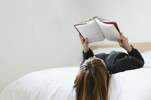 a woman lies on her bed reading a book.