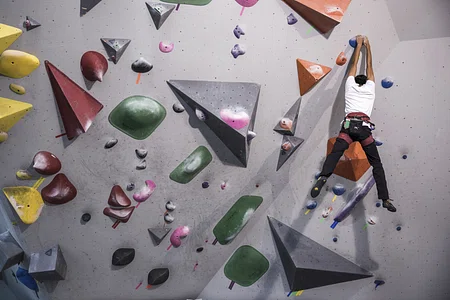 A person climbs a multi-coloured wall of shapes.