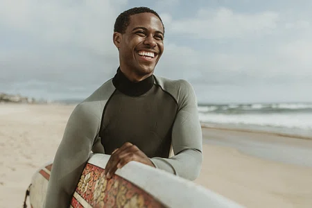 A man smiles as he carries his surfboard.